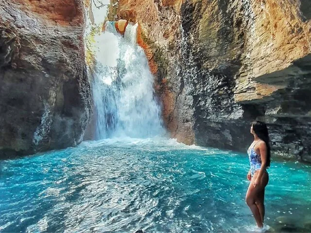 Woman in swimsuit standing in blue pool at La Leona Waterfall canyon.