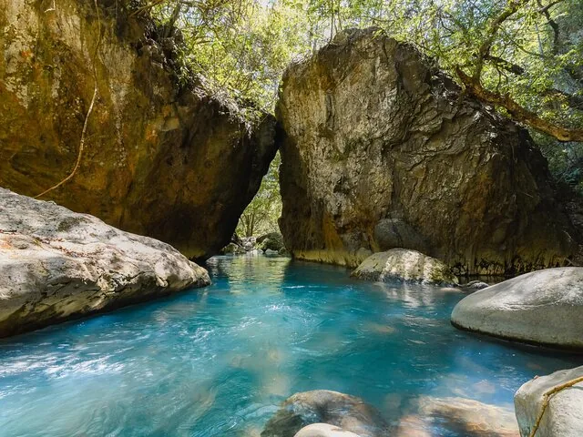 Blue river flowing between large boulders in a lush, rocky canyon.