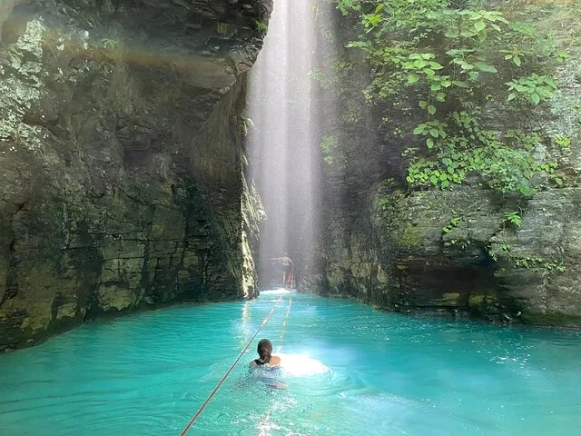 Persoon zwemt met een touw naar een heldere opening in een canyon.