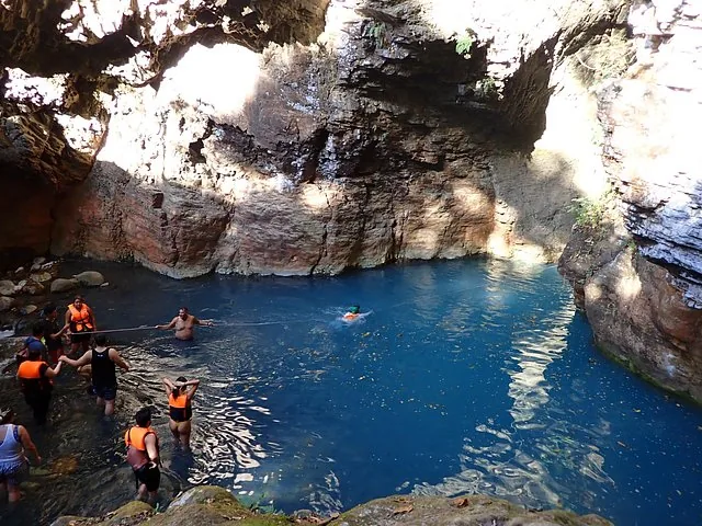 Groep mensen zwemt in een groot blauw bassin in een rotsachtige canyon.