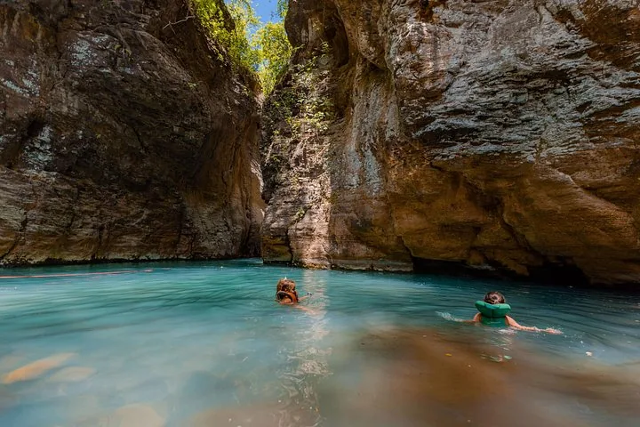 Twee mensen zwemmen met reddingsvesten in een turquoise rivier in een canyon.